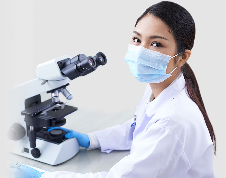 photo of female pharmaceutical professional wearing a mask looking through microscope